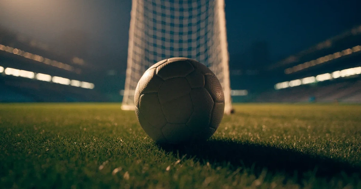 Ein Fußball liegt auf dem Rasen eines leeren Stadions bei Flutlicht, im Hintergrund unscharfe Tribünen ohne erkennbare Beschriftung.