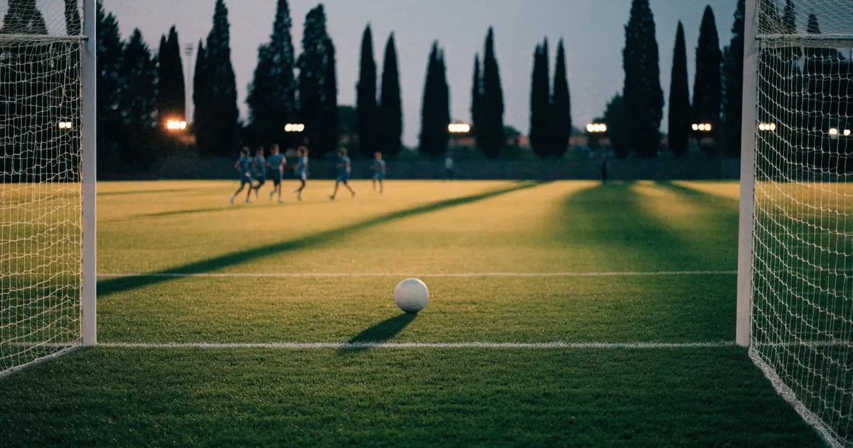 Ein Fußballtor mit Netz auf einem leeren Platz im Abendlicht, der Rasen frisch gemäht, im Hintergrund Zypressen.