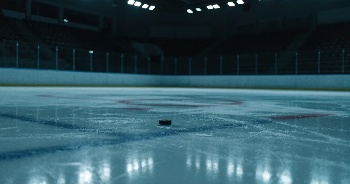 Eine leere Eisfläche in einer Halle mit Banden und Flutlicht, auf dem Eis liegt ein einzelner Puck.